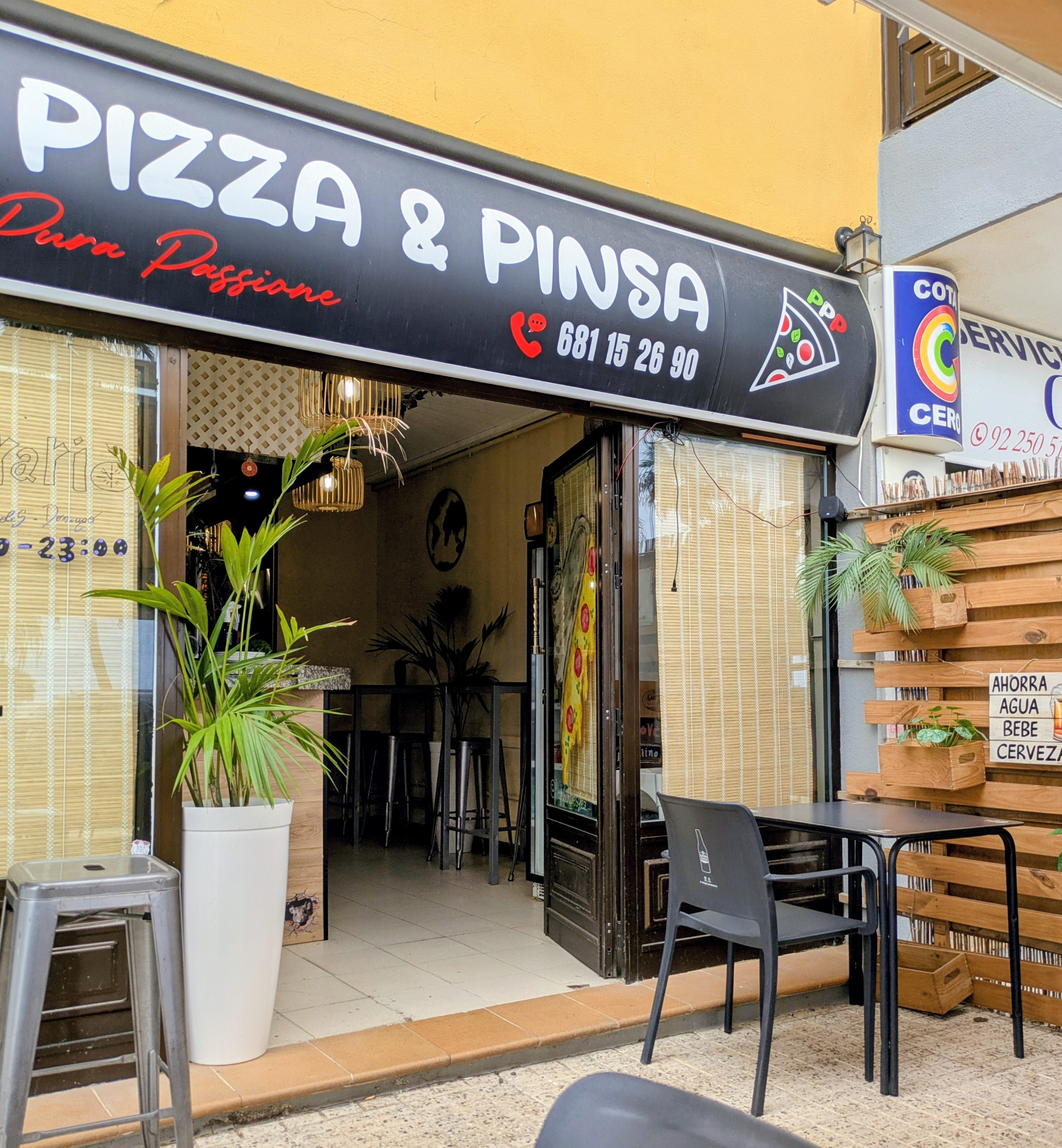 Fachada de Pizza & Pinsa Pura Passione con el rótulo negro, la puerta abierta y una mesa en la terraza