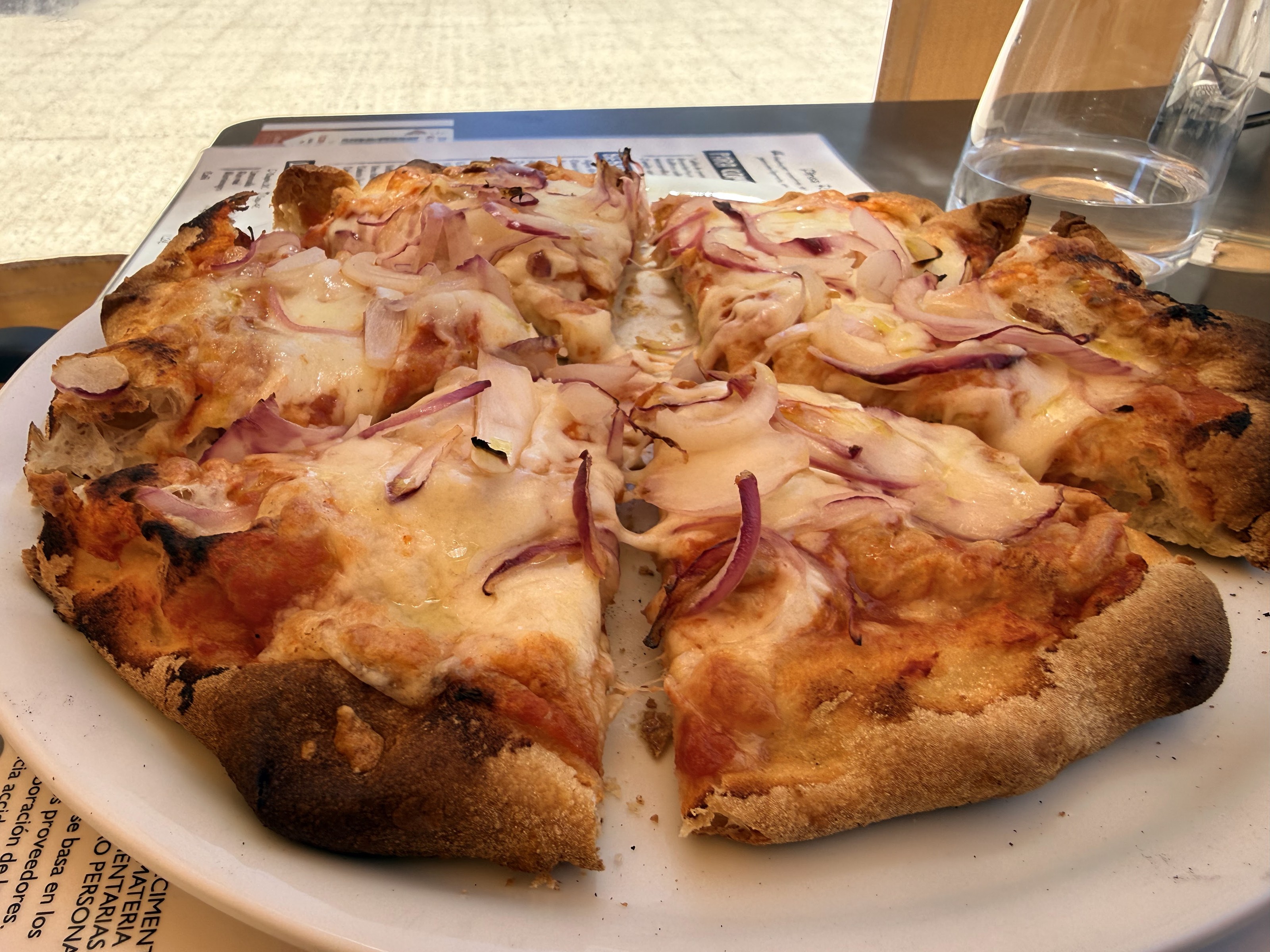 Pizza con cebolla roja y queso, cortada en porciones, junto a una jarra de agua