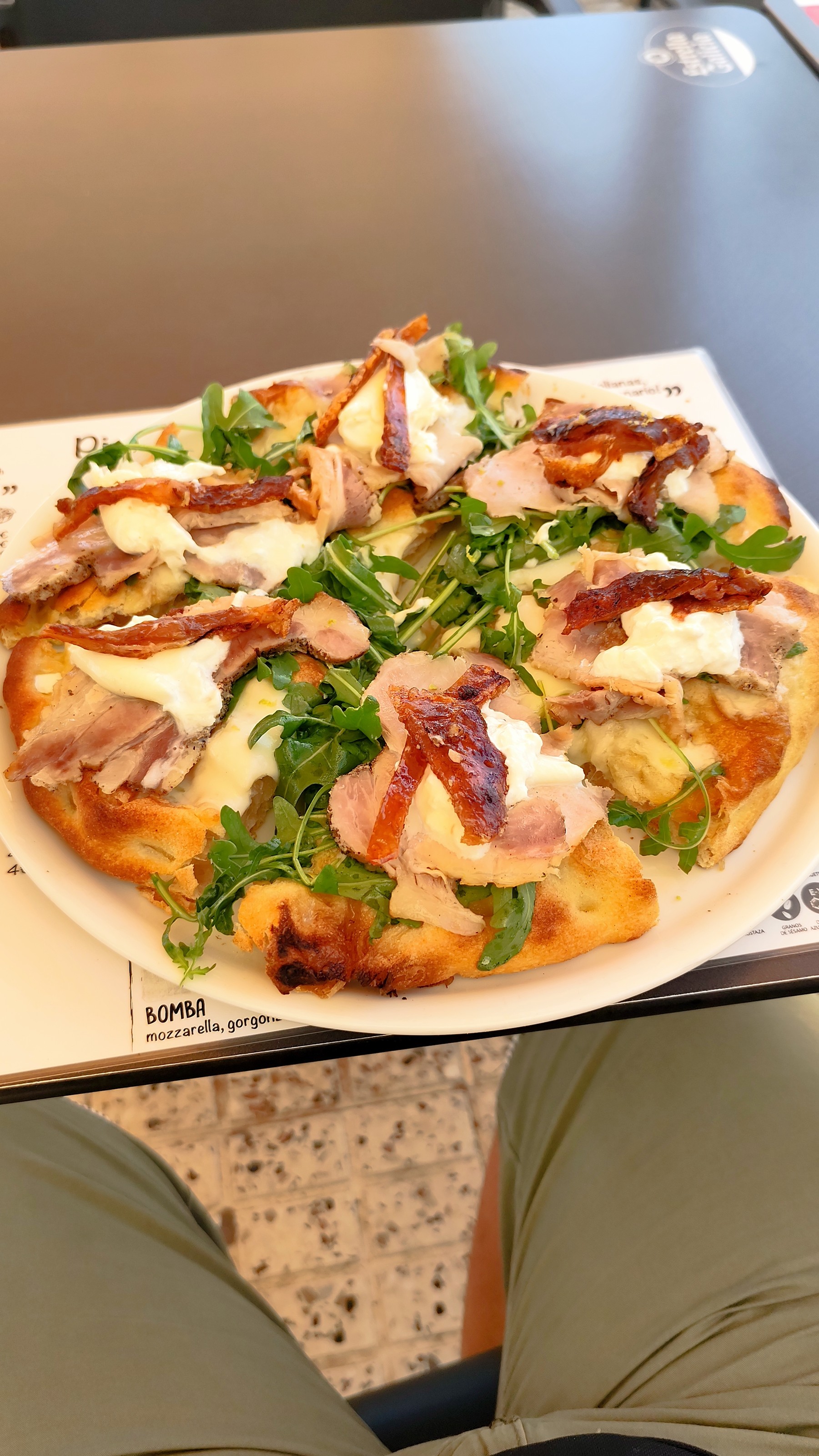 Pizza con jamón, burrata y rúcula sobre el mantel con la carta impresa