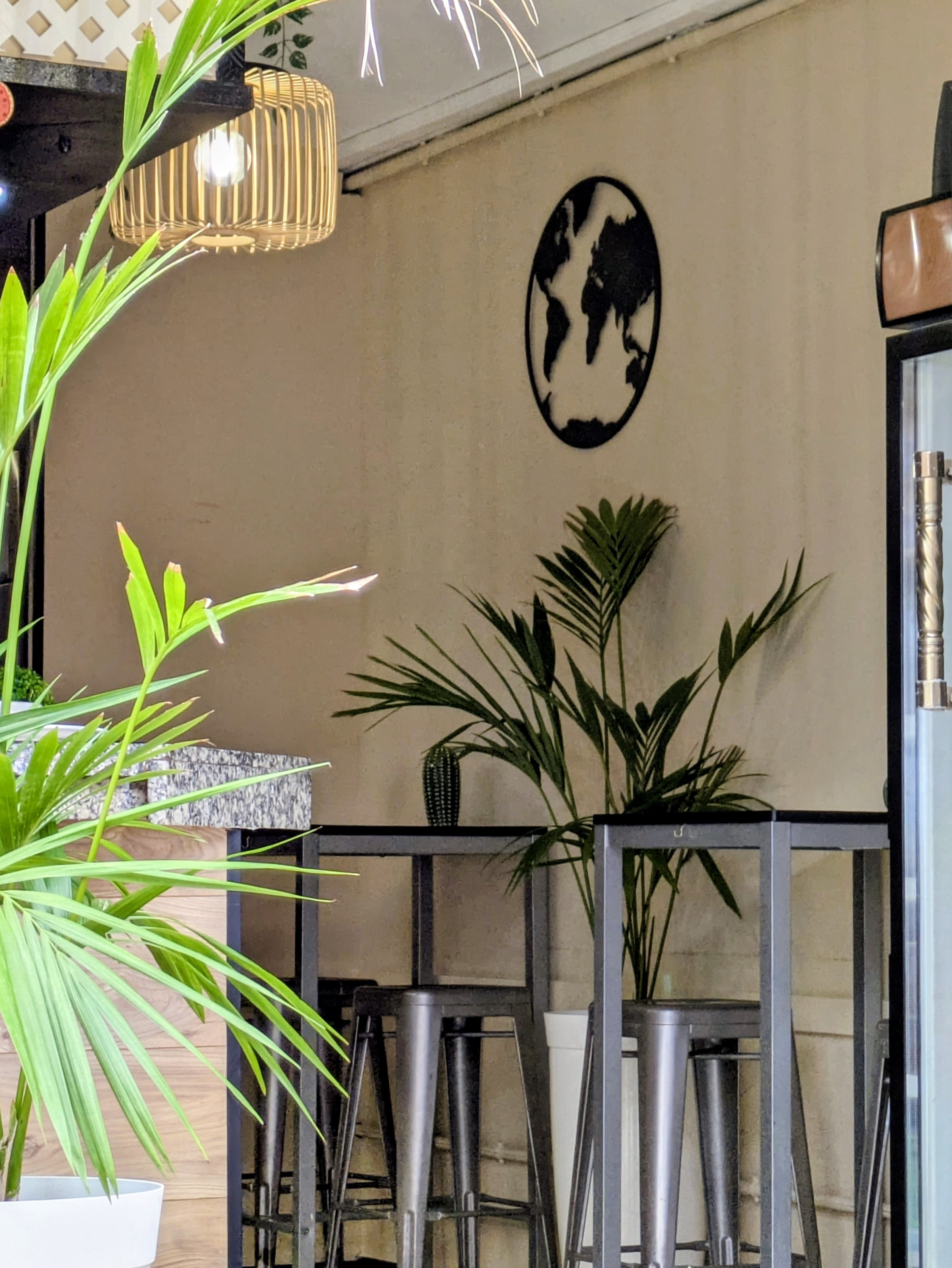 El interior: pared con un globo terráqueo negro, lámpara de mimbre, palmeras y taburetes