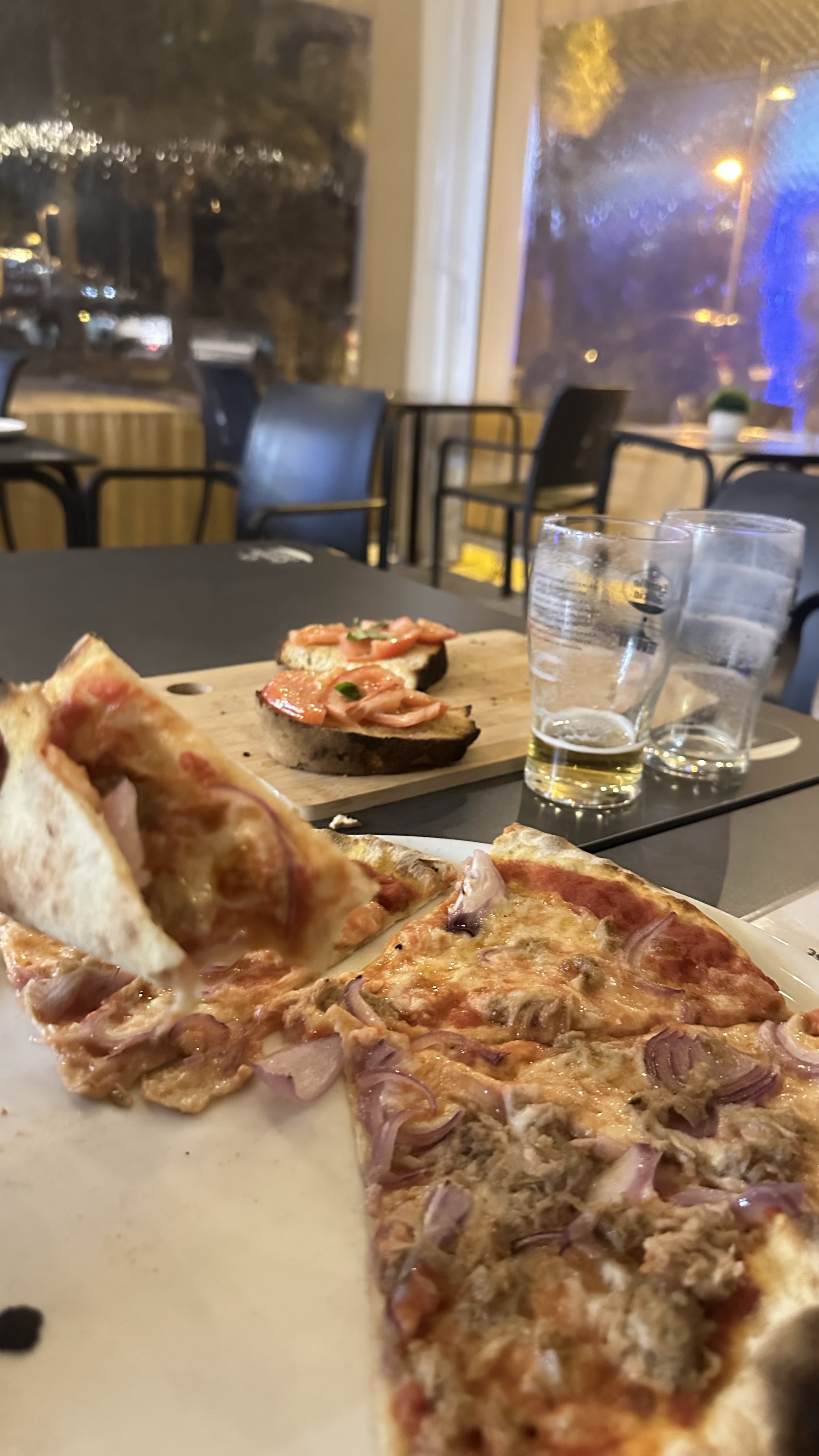 Pizza con atún y cebolla roja; detrás, bruschetta con tomate